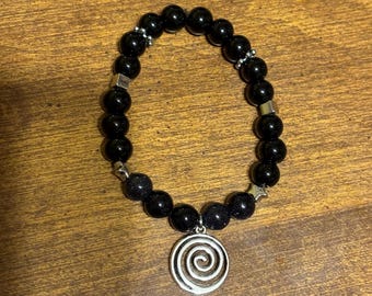 Könnte beinhalten: Schwarzes Perlenarmband mit einem silbernen Spiral-Anhänger. Die Perlen haben eine glitzernde Oberfläche.