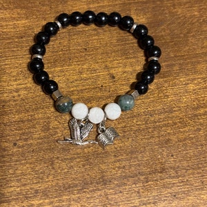 May include: Black beaded bracelet with green and white beads, a bird charm, and a book charm.