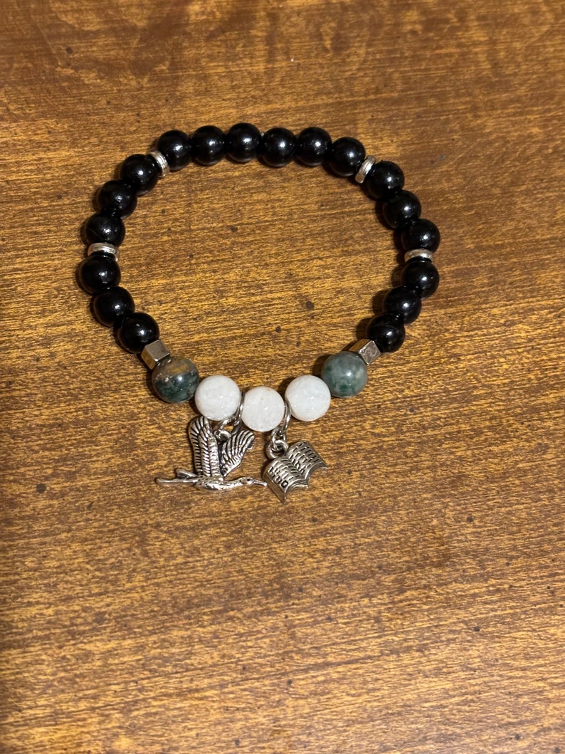 May include: Black beaded bracelet with green and white beads, a bird charm, and a book charm.