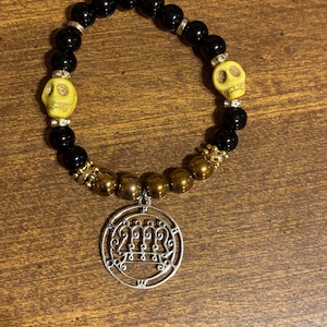 May include: A black beaded bracelet with yellow skull beads, gold and silver accents, and a silver pendant. The bracelet features a mix of black, gold, and silver beads, creating a gothic or alternative aesthetic.