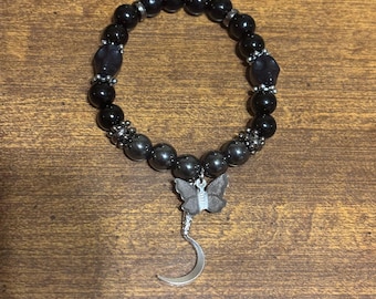 Op de afbeelding: Zwarte kralen armband met een zilveren halve maan en vlinder bedel.