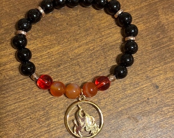 May include: Black beaded bracelet with red and orange beads and a gold charm of a flame.