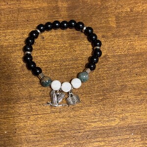 May include: Black beaded bracelet with green and white beads and silver charms of a bird and an open book.