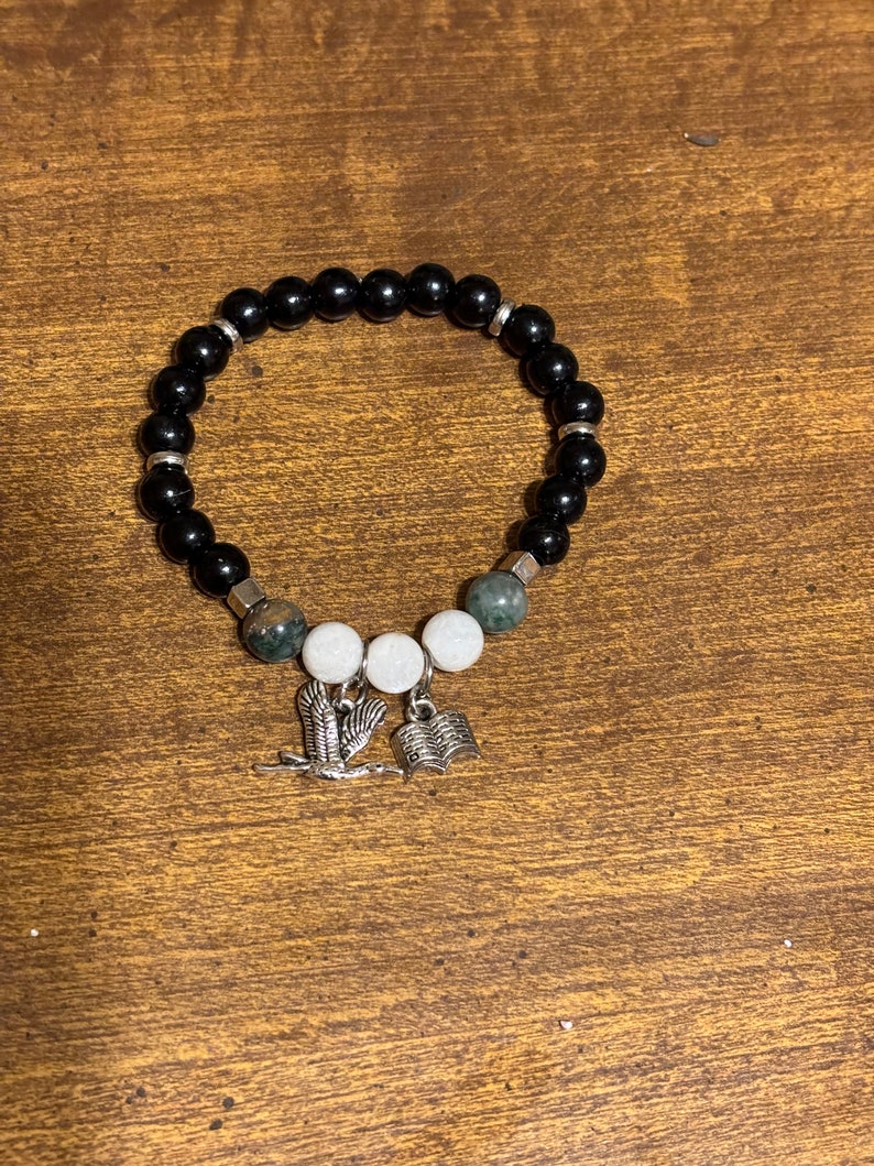 May include: Black beaded bracelet with green and white beads and silver charms of a bird and an open book.