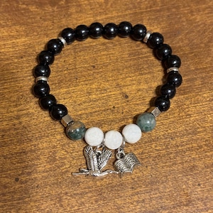 May include: Black beaded bracelet with green and white beads and silver charms of a bird and an open book.