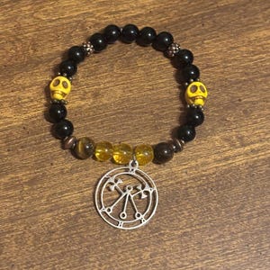 May include: Black beaded bracelet with yellow skull accents and a silver pendant. The bracelet features black and yellow beads, with a silver charm. The bracelet is approximately 7 inches in circumference.