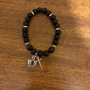 May include: Black beaded bracelet with gold accents and a silver crown and sword charm.