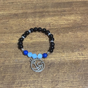 May include: A beaded bracelet featuring black, blue, and light blue beads. The bracelet has a silver-colored charm with a unique design. The beads are strung together with silver-colored spacers. The bracelet is a stylish accessory.
