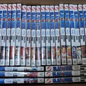 Puede incluir: Una colección de volúmenes de manga, con lomos blancos con detalles en azul y rojo. Los lomos muestran los números 1-25, junto con el título y el nombre del autor. La fila inferior incluye los volúmenes 26-31.