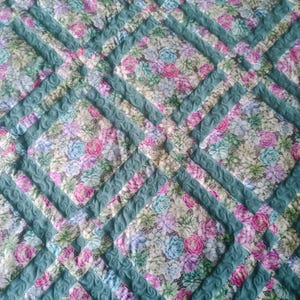 Pode incluir: Uma colcha turquesa e branca com um padrão floral. A colcha é acolchoada com um ponto decorativo que se assemelha a um redemoinho.