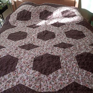May include: A brown and pink quilt with a hexagonal pattern. The quilt is made of different fabrics and has a quilted texture.