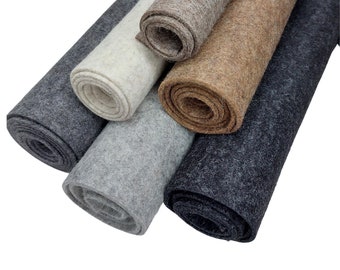 May include: A collection of rolled felt fabric in various neutral colors. The rolls include shades of gray, beige, and off-white, showcasing the texture and color variations of the material. The felt appears to be thick and suitable for crafts.