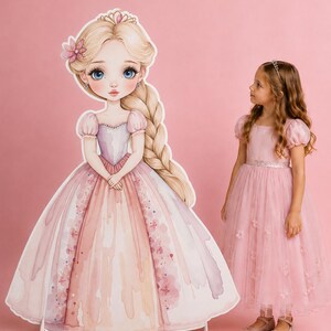 May include: A young girl stands beside a large cardboard cutout of a princess. The princess has blonde hair, a pink dress, and a tiara. The girl wears a pink dress and a tiara. The background is pink.