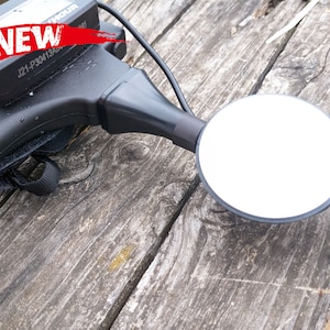 May include: A black metal detector with a round, white search coil. The detector has a black handle with a strap and a control panel with the text "NEW" and "J21-P30413401".