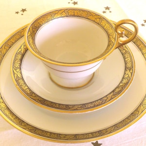 Könnte beinhalten: Ein weißes Tee-Set mit goldener Blumenmuster. Die Teetasse hat eine abgerundete Form und einen Henkel. Die Untertasse hat einen gewellten Rand.