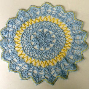 Könnte beinhalten: Eine gehäkelte Deckchen in Blau und Gelb mit einem zarten Blumenmuster.