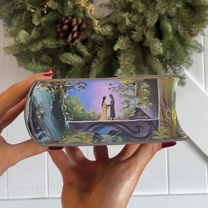 May include: A hand-painted book cover with a whimsical scene of a couple standing on a bridge in a forest. The background is a vibrant purple and blue sky with a waterfall in the distance. The book cover is painted in a realistic style with intricate details.