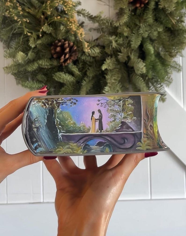 May include: A hand-painted book cover with a whimsical scene of a couple standing on a bridge in a forest. The background is a vibrant purple and blue sky with a waterfall in the distance. The book cover is painted in a realistic style with intricate details.