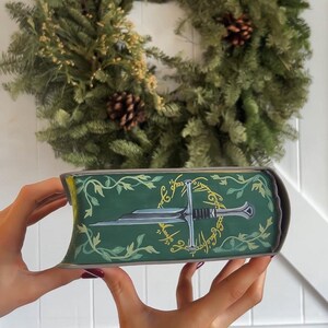 May include: A green book with a gold inscription and a silver sword design. The inscription reads "One Ring to rule them all, One Ring to find them, One Ring to bring them all and in the darkness bind them."