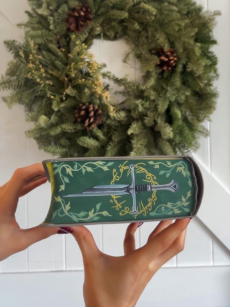 May include: A green book with a gold inscription and a silver sword design. The inscription reads "One Ring to rule them all, One Ring to find them, One Ring to bring them all and in the darkness bind them."