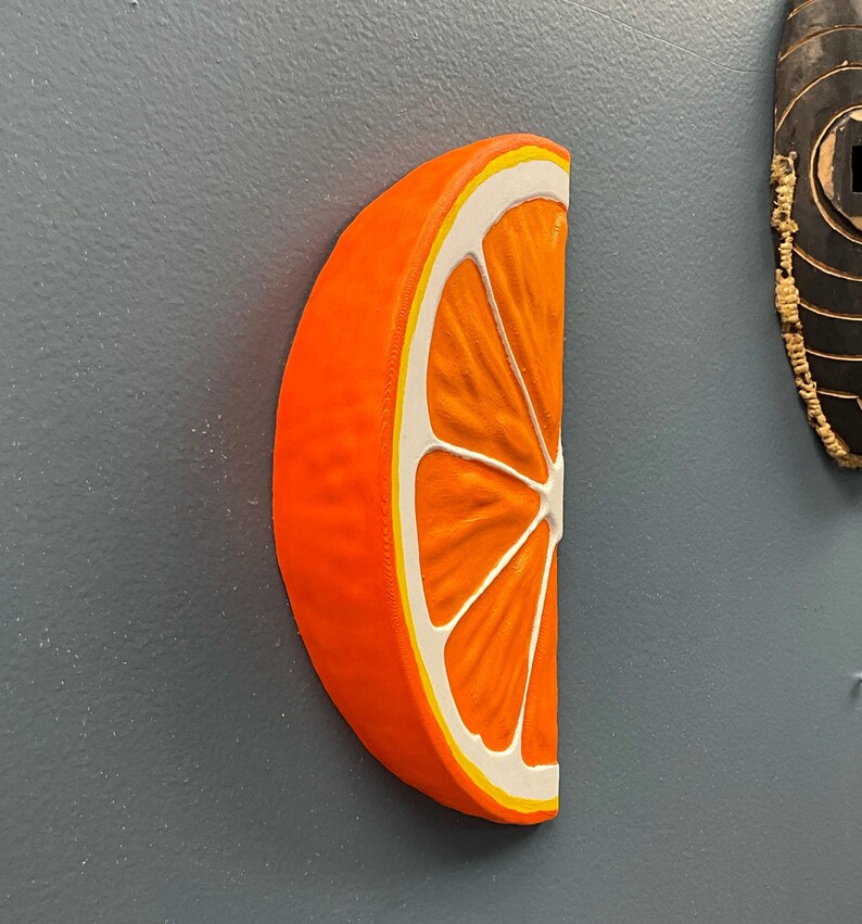 May include: A vibrant orange, half-slice of an orange with white and yellow accents. The fruit is displayed against a gray background. The image showcases a detailed, three-dimensional representation of the citrus fruit.