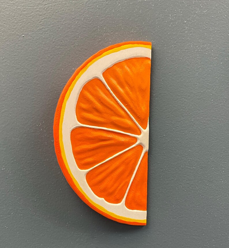 May include: A half-slice of an orange, featuring a bright orange interior with white and yellow accents. The fruit's segments are clearly defined, and the rind is detailed with a yellow and white border. The image is set against a gray background.
