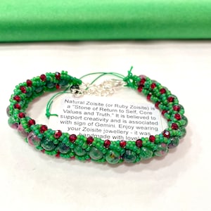 May include: A green and red beaded bracelet made with natural zoisite and ruby zoisite gemstones. The bracelet is handmade and comes with a tag that reads "Natural Zoisite (or Ruby Zoisite) is a "Stone of Return to Self, Core Values and Truth." It is believed to support creativity and is associated with sign of Gemini. Enjoy wearing your Zoisite jewellery - it was handmade with love"