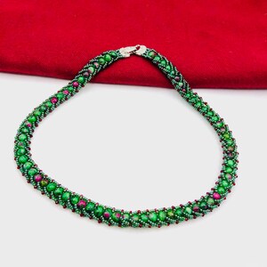 May include: A green and red beaded necklace with a silver clasp. The beads are small and round, and they are arranged in a spiral pattern.