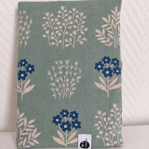 Könnte beinhalten: Eine grüne Stofftasche mit einem Blumenmuster mit blauen Blüten und weißen Stielen. Die Tasche hat ein kleines weißes Etikett mit dem Text "ME & Co.s".