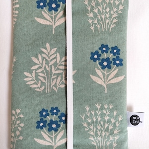 Könnte beinhalten: Eine grüne Stofftasche mit einem weißen Reißverschluss und einem floralen Muster in Blau und Weiß. Die Tasche hat ein Etikett mit der Aufschrift "ME & Cosima".