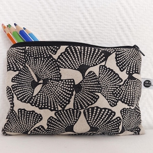 Könnte beinhalten: Schwarz-beige Federtasche mit einem sich wiederholenden fächerartigen Muster. Die Tasche ist mit mehreren Buntstiften gefüllt. Ein kleines Etikett mit Text ist an der Seite befestigt.