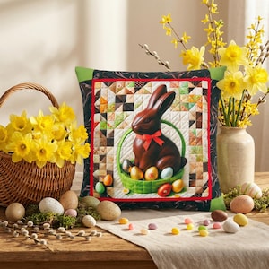Könnte beinhalten: Ein dekoratives Osterkissen mit einem Schokoladenhasen mit roter Schleife in einem grünen Korb voller bunter Eier. Das Kissen hat ein Patchwork-Design und einen schwarzen Rand. Ein Weidenkorb mit gelben Blumen befindet sich links.