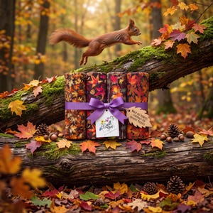 Może przedstawiać: Cztery rolki tkaniny w jesienne liście, związane fioletową wstążką z etykietą o treści Quill Shop i Magie des Herbstes - Stoffpaket für kreative Projekte, spoczywające na omszałej kłodzie z wiewiórką znajdującą się powyżej.