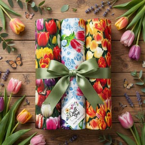 May include: Three rolls of fabric tied with a green ribbon and bow. The fabric features tulip patterns in red, yellow, and white. The label reads "Quilt Shop Ruth Baudisch". Butterflies and tulips are arranged around the fabric.
