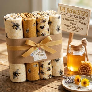 Könnte beinhalten: Ein Set aus Baumwollstoffen mit Bienenmotiven, verpackt mit einem goldenen Band. Das Set enthält vier Stoffrollen mit Bienen- und Wabenmustern. Ein Schild trägt die Aufschrift "The Beekeeper's Curated Cotton Bundle". Honig und eine Honigwabe sind ebenfalls zu sehen.