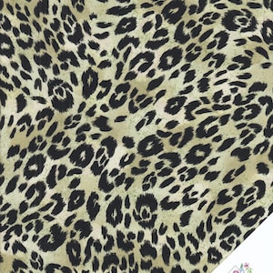 Pode incluir: Um tecido bege com um padrão de estampa de leopardo preto. O tecido tem um brilho sutil.