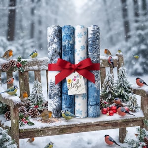 Pode incluir: Quatro rolos de tecido com padrões de inverno de florestas nevadas e flocos de neve azuis, amarrados com uma fita vermelha e uma etiqueta branca com a inscrição Quilt Shop, dispostos verticalmente num banco de madeira coberto de neve.