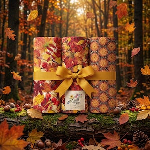 Könnte beinhalten: Drei Stoffrollen, die mit einem senfgelben Band zusammengebunden sind. Die Rollen zeigen herbstliche Muster aus roten, orangen und gelben Blättern sowie ein geometrisches Blumenmuster. Ein weißes Etikett trägt die Aufschrift Quilt Shop Ruth Baudisch.