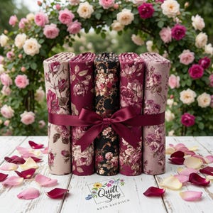 Könnte beinhalten: Gerollte Stoffbündel mit floralen Mustern in Burgunderrot, Creme und Schwarz, gebunden mit einem burgunderfarbenen Band. Der Hintergrund zeigt einen Rosenbogen und verstreute Blütenblätter. Das Logo von Quilt Shop by Ruth Baudisch ist sichtbar.