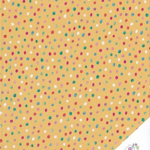 Könnte beinhalten: Senfgelber Stoff mit einem sich wiederholenden Muster aus bunten Punkten. Die Punkte sind in den Farbtönen Rot, Blau, Grün, Lila und Weiß gehalten. Eine Ecke des Stoffes zeigt ein Logo mit der Aufschrift "Quilt Shop Ruth Baudisch".