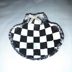 May include: A shell-shaped decorative dish featuring a black and white chequered pattern. The edges are silver, and a small white bow adorns the top. Ideal for holding small items, this dish is unique.