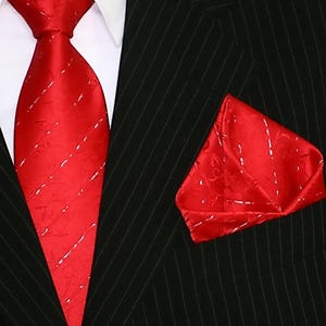 Könnte beinhalten: Ein rotes Seidenkrawatten- und Einstecktuch-Set mit Muster. Die Krawatte hat ein weißes Muster auf rotem Grund. Das Einstecktuch hat ein ähnliches Muster.