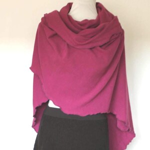 May include: A magenta-colored shawl draped over a white mannequin head. The shawl has a draped cowl neck and a scalloped edge. A black skirt is visible below the shawl. The background is plain white.