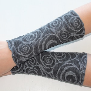 Könnte beinhalten: Ein Paar dunkelgraue Armstulpen mit einem wirbelnden, floralen Muster. Der Stoff scheint ein weiches Strickmaterial zu sein. Die Armstulpen werden an den Armen einer Person gezeigt, wobei die Handgelenke und Unterarme bedeckt sind.