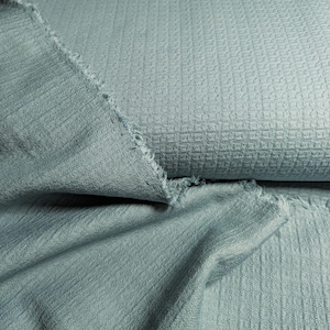 Peut inclure: Deux morceaux de tissu bleu doux à armure texturée. Le tissu est plié et drapé, montrant la texture et la couleur.