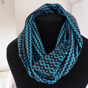 Könnte beinhalten: Blau-brauner Infinity-Schal mit sich wiederholendem geometrischen Muster. Der Schal wird auf einer schwarzen Schaufensterpuppe präsentiert, die sein Design und seine Textur hervorhebt. Das Muster umfasst Zickzack- und Kreisformen.