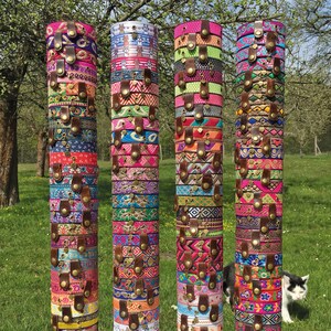 May include: A display of colorful bracelets made from woven fabric and decorated with metal accents. The bracelets are stacked on wooden poles and arranged in four columns.