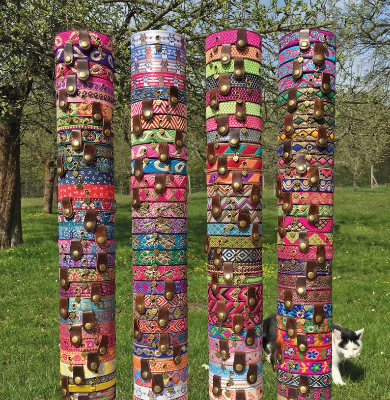May include: A display of colorful bracelets made from woven fabric and decorated with metal accents. The bracelets are stacked on wooden poles and arranged in four columns.