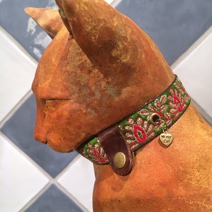 May include: A terracotta cat figurine wearing a green, red, and gold embroidered collar with a small metal tag that says "I love my cat".