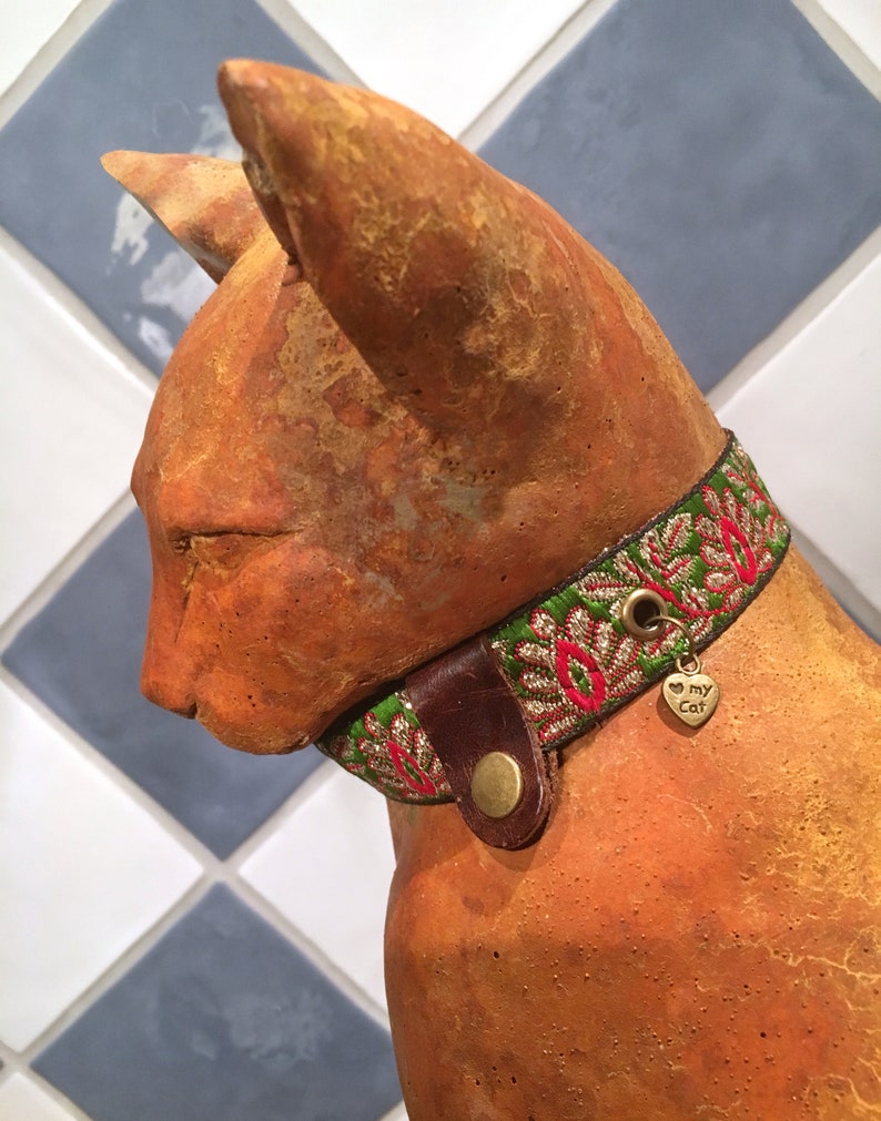 May include: A terracotta cat figurine wearing a green, red, and gold embroidered collar with a small metal tag that says "I love my cat".